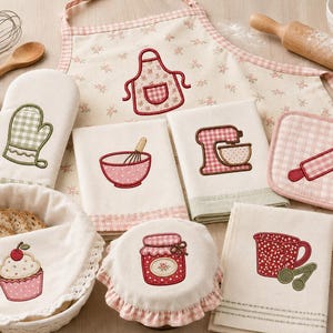 Könnte beinhalten: Ein Küchentextil-Set bestehend aus Schürze, Ofenhandschuh, Topflappen und Geschirrtüchern mit Stickereien von Cupcake, Marmeladenglas, Schneebesen, Schüssel, Mixer und Messlöffeln auf cremefarbenem Stoff mit rosa und grünen Karomustern.
