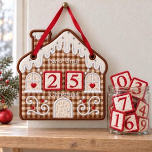 Könnte beinhalten: Ein Lebkuchenhaus-Adventskalender aus Stoff mit braun-weißem Karomuster, weißer Verzierung und rotem Aufhänger. Der Text lautet Days Until Christmas. Zwei quadratische Felder zeigen die Zahl 25, weitere nummerierte Plättchen befinden sich in einem Glas.