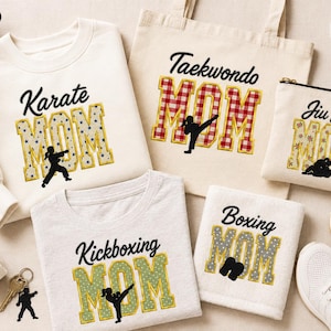 Puede incluir: Una colección de ropa y accesorios de color crema que incluye una sudadera, una bolsa de tela, un estuche con cremallera y una toalla. Cada artículo presenta textos como Karate, Taekwondo, Jiu Jitsu o Kickboxing Mom con un artista marcial.