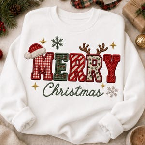 Op de afbeelding: Een wit sweatshirt met lange mouwen en de tekst MERRY in grote, veelkleurige blokletters, met een rode kerstmuts op de M en bruine rendiergeweien op de R. Het woord Christmas staat eronder in een donkergroen cursief lettertype.