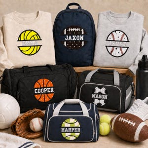 May include: A collection of personalized sports-themed gear including a beige sweatshirt with a yellow volleyball, a navy backpack with a football, a gray sweatshirt with a baseball, two black duffel bags with basketball and soccer ball designs, and a navy duffel bag with a green checkered ball, all featuring names.