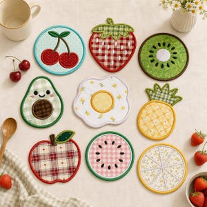 Può includere: Un set di nove sottobicchieri in tessuto con ricami raffiguranti ciliegia, fragola, kiwi, avocado, uovo al tegamino, ananas, mela, anguria e fetta di agrume. Ogni sottobicchiere presenta motivi distinti tra cui quadretti vichy, fiori e pois.