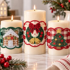 May include: Three cream-colored pillar candles, each lit and wrapped in a decorative fabric band. The left candle features a gingerbread house, the center candle displays a wreath with a red bow and gold bells, and the right candle shows a Christmas tree.