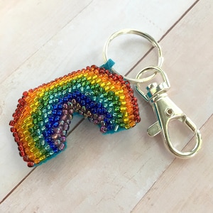 May include: A rainbow-colored beaded keychain with a silver key ring and clasp. The rainbow is made of small, colorful beads and is attached to a turquoise felt backing.