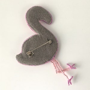 May include: A pink beaded flamingo brooch with a gray felt backing and a metal pin closure.