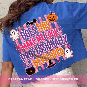 May include: A bright blue t-shirt featuring a graphic print with the text DOES THIS MAKE ME LOOK PROFESSIONALLY DEVELOPED in orange and purple. The design includes a pumpkin, ghosts, a black cauldron, a witch hat, bats, and stars.