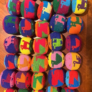 May include: A collection of forty-two round, crocheted hacky sacks arranged in a grid. Each ball features a multi-colored, geometric animal pattern, including various combinations of red, blue, green, yellow, orange, purple, and pink yarn.