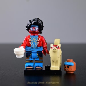 Peut inclure: Une figurine de bloc de construction en plastique avec des cheveux noirs, un masque rouge et un torse rouge orné d'un emblème d'araignée doré. Elle porte un pantalon bleu avec une ceinture, tient une tasse blanche et est accompagnée d'un chat beige.
