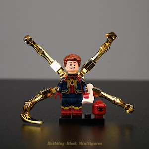 Op de afbeelding: Een plastic bouwsteen-minifiguur met een bruinharig personage in een blauw en rood pak met vier metalen gouden mechanische armen die vanaf de rug uitsteken. Een losse rode kop met een zwart spinnenembleem staat op een zwarte basis.