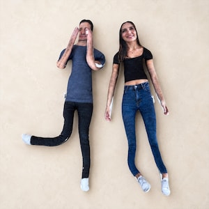 May include: Two custom fabric dolls featuring printed photographic faces. The left doll wears a gray t-shirt and black pants. The right doll wears a black short-sleeved top and blue denim jeans. Both dolls have light-colored fabric hands and feet.