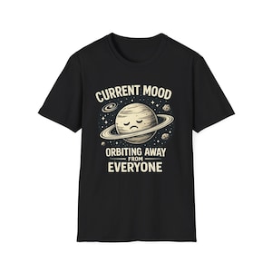 May include: Black t-shirt with a graphic featuring a planet with a sad face, surrounded by rings and stars. Text reads "CURRENT MOOD ORBITING AWAY FROM EVERYONE" in white, creating a humorous and relatable design.