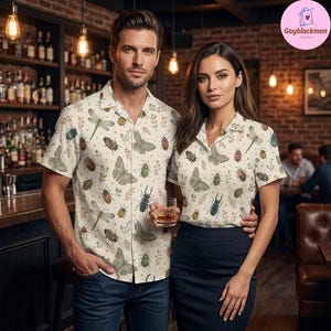 May include: A short-sleeved button-down shirt featuring an all-over print of various insects, including dragonflies, beetles, and moths, interspersed with small green sprigs on a light cream-colored fabric with a classic collar and front buttons.