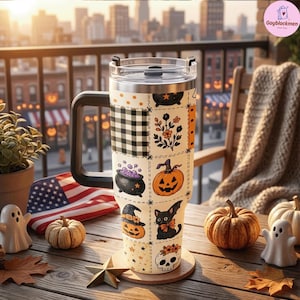 May include: A tall, cream-colored insulated tumbler with a black handle and lid, featuring a patchwork pattern of Halloween icons including pumpkins, a black cat, a skull, a cauldron with purple bubbles, and black and white buffalo plaid squares.