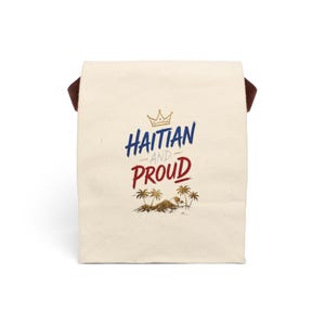 May include: A cream-colored canvas lunch bag with brown side straps. The front features a gold crown icon above the blue text HAITIAN, the gray word AND, and the red text PROUD, followed by a graphic of palm trees and a small mountain range.
