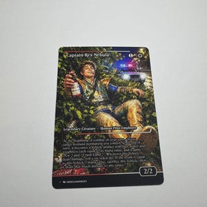 May include: A rectangular trading card titled Captain Rex Nebula featuring a colorful illustration of a person lying in green foliage holding a bottle, with a police car in the background. The card includes game text, mana symbols, and a 2/2 power rating.