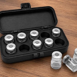 May include: A black rectangular storage case with a hinged lid containing six clear glass vials with silver metal caps. Three additional empty glass vials with silver caps are positioned outside the case, which features molded slots.