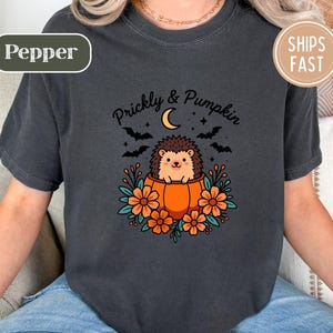 Dark gray t-shirt showing a hedgehog in a pumpkin, with text "Prickly & Pumpkin" and other graphics.