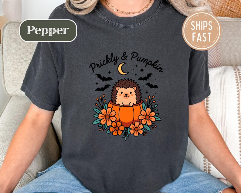 Dark gray t-shirt showing a hedgehog in a pumpkin, with text "Prickly & Pumpkin" and other graphics.