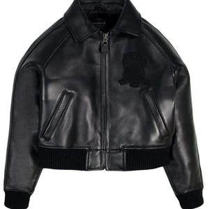May include: A black leather bomber jacket featuring a classic collar, a full-length front zipper closure, and two slanted side pockets. The jacket includes black ribbed knit cuffs and a matching ribbed hem, with a tonal embroidered patch on the chest.