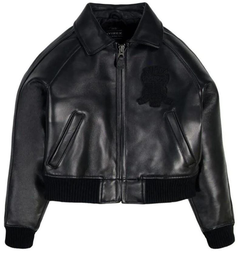 May include: A black leather bomber jacket featuring a classic collar, a full-length front zipper closure, and two slanted side pockets. The jacket includes black ribbed knit cuffs and a matching ribbed hem, with a tonal embroidered patch on the chest.