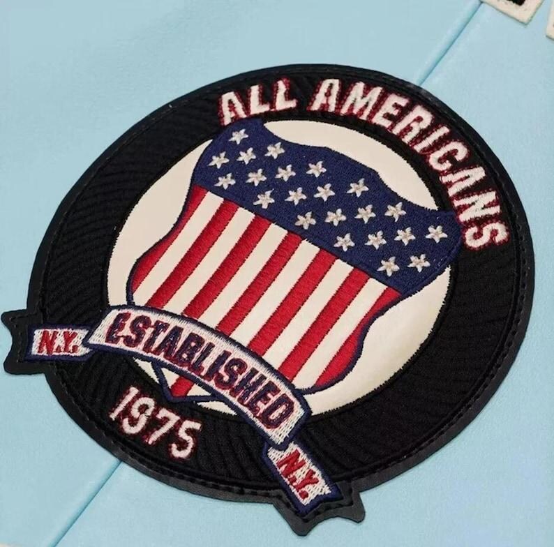 Pu&ograve; includere: Una toppa ricamata circolare su sfondo azzurro raffigurante uno scudo con strisce rosse e bianche e un campo blu con stelle bianche. Il testo ALL AMERICANS, ESTABLISHED 1975 e N.Y. &egrave; ricamato in rosso e bianco su un bordo nero.