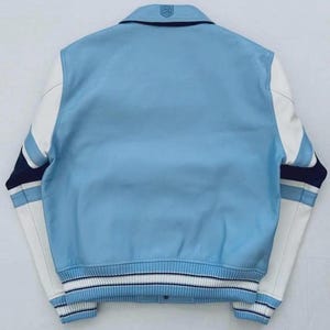 Op de afbeelding: Een lichtblauw varsity-jack met witte leren mouwen, een geribbelde kraag en gestreepte boorden in lichtblauw, wit en marineblauw. Het achterpand is effen lichtblauw met een klein reli&euml;flogo in het midden van de kraag.