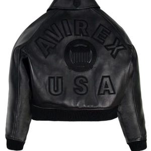 May include: A black leather jacket featuring a collar and ribbed cuffs and hem. The back displays the embossed text AVIREX USA in a curved arrangement above a circular emblem with vertical stripes, all in a matching black tone on the leather.