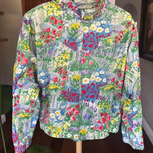 May include: A long-sleeve zip-up jacket featuring a vibrant, multi-colored floral and garden-inspired print. The pattern includes shades of red, yellow, blue, and green, with a high collar, elasticized cuffs, and a straight hemline.