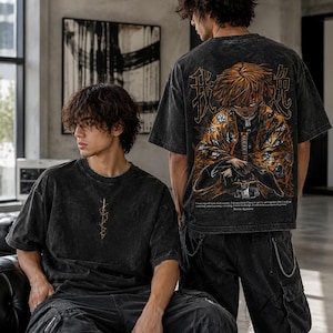 May include: A black acid-wash t-shirt featuring a small gold graphic on the chest and a large, detailed anime character illustration on the back. The back design includes orange and yellow accents, Japanese kanji characters, and English text.
