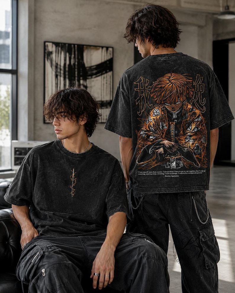 May include: A black acid-wash t-shirt featuring a small gold graphic on the chest and a large, detailed anime character illustration on the back. The back design includes orange and yellow accents, Japanese kanji characters, and English text.