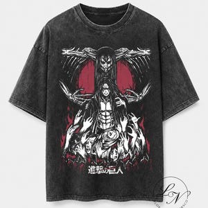 Puede incluir: Una camiseta gris carbón con efecto lavado al ácido que presenta un estampado gráfico de una figura central de pelo largo rodeada de manos esqueléticas sobre un fondo circular rojo. El texto japonés "進撃の巨人" aparece en la parte inferior.