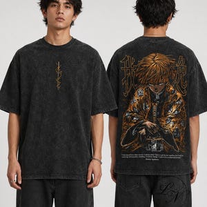 May include: A charcoal grey acid-wash t-shirt featuring a small vertical sword graphic on the front. The back displays a large, detailed orange and black anime character illustration with Japanese kanji and English text at the bottom.