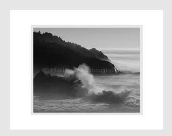 May include: A black and white photograph of a rocky coastline with crashing waves. The waves are breaking against the rocks and creating a spray of water. The sky is cloudy and the water is choppy.