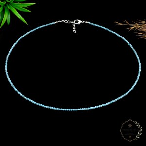 May include: A delicate necklace composed of small, round, light blue beads strung together. The necklace features a silver-toned metal lobster claw clasp and an adjustable chain link extension at the back for a secure and customizable fit.