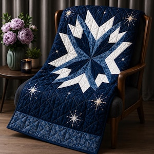 Puede incluir: Una colcha azul marino con un gran patrón de estrella en blanco y azul con pequeños detalles de estrellas doradas. La tela tiene una textura acolchada de diamantes y un borde decorativo en la parte inferior con un sutil diseño de hojas.