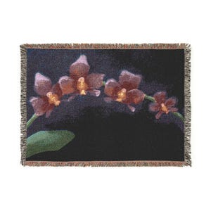 Peut inclure: Un plaid tissé rectangulaire présentant un fond noir sombre avec une branche horizontale de quatre orchidées en fleurs violettes et orange. La couverture possède un bord texturé à franges sur les quatre côtés, révélant un tissage en tapisserie.