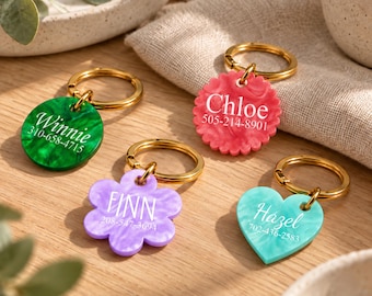May include: Four acrylic pet tags with gold-tone metal rings. A green circle reads Winnie 310-658-4715, a pink scalloped circle reads Chloe 505-214-8901, a purple flower shape reads FINN 208-547-3694, and a teal heart reads Hazel 702-436-2583.