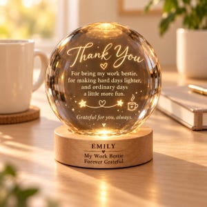 May include: A spherical glass night light with an amber glow, featuring the engraved text: Thank You, For being my work bestie, for making hard days lighter, and ordinary days a little more fun. Grateful for you, always. It sits on a wooden base with EMILY, My Work Bestie, Forever Grateful.