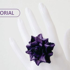 Puede incluir: Un anillo de flor de cuero morado. El anillo se lleva en una mano de maniquí blanca.