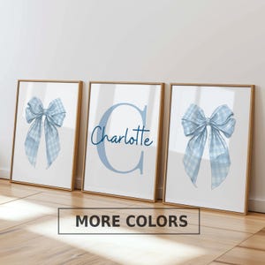 May include: Three framed wall art prints with light wooden frames. The two outer prints feature a light blue and white gingham patterned bow. The center print displays a large light blue letter C with the name Charlotte written in blue script.