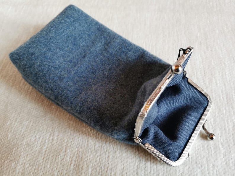 Puede incluir: Un estuche rectangular de fieltro azul con un cierre de boquilla met&aacute;lico de color plateado. El interior del estuche est&aacute; forrado con una tela azul oscuro y el exterior tiene una superficie suave y texturizada propia del fieltro.
