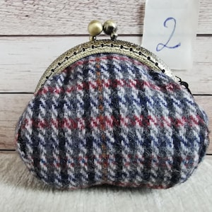 May include: A coin purse featuring a blue, grey, white, and red plaid wool-like fabric pattern. The purse has a curved, antique-style brass metal frame with a kiss-lock closure topped with two small, round, metallic beads. The number 2 is visible.