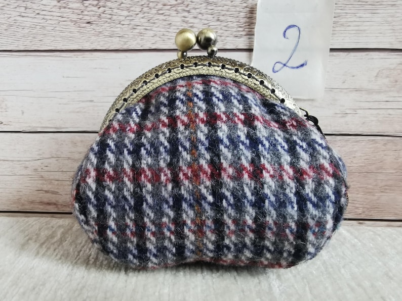 May include: A coin purse featuring a blue, grey, white, and red plaid wool-like fabric pattern. The purse has a curved, antique-style brass metal frame with a kiss-lock closure topped with two small, round, metallic beads. The number 2 is visible.