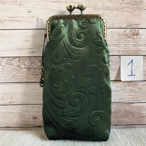 Puede incluir: Un bolso rectangular vertical de tela verde bosque profundo con un patr&oacute;n floral en relieve. El bolso cuenta con un marco de metal color bronce con un cierre de boquilla de dos botones y una peque&ntilde;a anilla lateral para colgar.