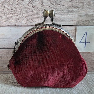 May include: A deep red velvet coin purse with a textured, antique bronze-toned metal frame and a dual-ball clasp closure. A small white paper tag with the handwritten number 4 is attached to the side of the frame, featuring a decorative edge.