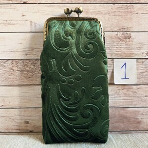 Puede incluir: Un estuche rectangular de color verde oscuro con un patr&oacute;n floral en relieve. El estuche tiene un marco met&aacute;lico de tono bronce con un cierre de doble bola en la parte superior. Se observa una peque&ntilde;a etiqueta cuadrada blanca con el n&uacute;mero 1.