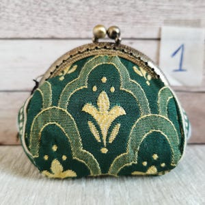 May include: A small coin purse featuring a dark green fabric with a repeating yellow floral pattern. The purse has a metallic bronze-toned kiss-lock clasp closure at the top. A small white square tag with the handwritten number 1 is visible.