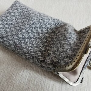 Puede incluir: Un estuche rectangular hecho de tela de tweed moteada en gris y blanco. El estuche cuenta con un marco de metal con cierre de boquilla en tono lat&oacute;n antiguo, con un patr&oacute;n decorativo en relieve y dos pomos esf&eacute;ricos en la parte superior.