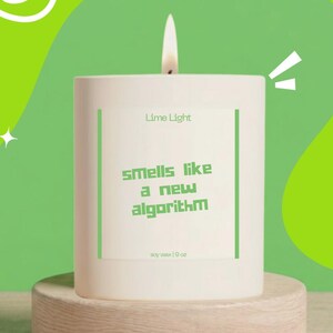 May include: A white cylindrical soy wax candle with a lit wick. The label features the text Lime Light and Smells like a new algorithm in green font, with soy wax 9 oz printed at the bottom. The candle is positioned on a round wooden base.