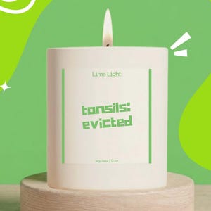 May include: A white cylindrical candle with a lit wick, featuring a label that reads Lime Light, tonsils: evicted, and soy wax 9 oz. The candle is positioned on a light-colored wooden circular base against a bright green background.